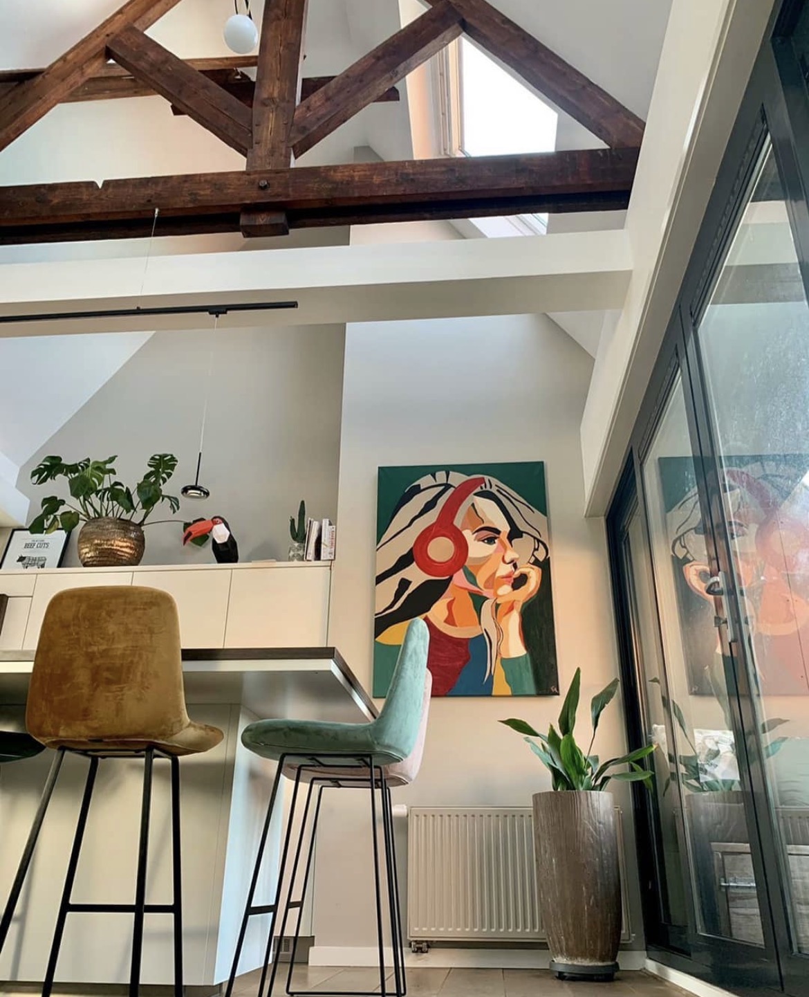 Colourful portrait painting with red headphones hanging in a bright loft interior with wooden beams
